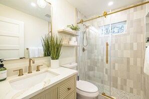 A bathroom with a white sink, gold fixtures, a glass shower enclosure, and a window with a view.