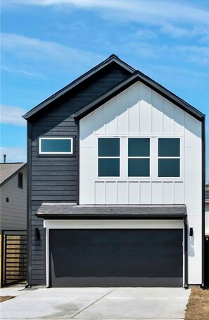 Ein zweistöckiges Haus mit Garage, einem kleinen Fenster im oberen Stockwerk und blauem Himmel.