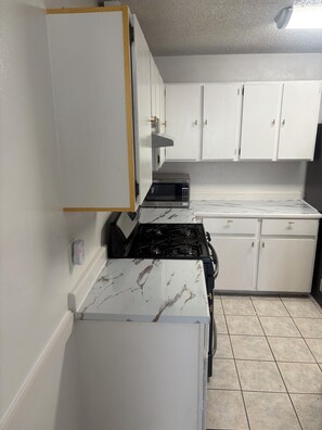 Een keuken met witte kastjes, een zwarte kookplaat en een marmeren aanrecht.