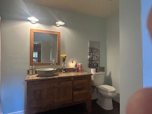 Ett badrum med ett handfat i trä, en stor spegel, en tvättställ, en toalett och en väggmonterad lampa.