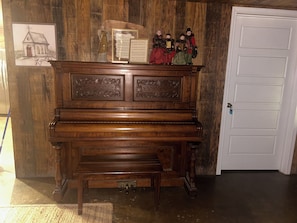 Un piano en bois, accompagné d’un banc, d’une porte et de décorations murales comprenant un dessin d’église et un tableau encadré.