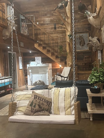 A rustic interior with a wooden staircase, a hanging swing chair, a sofa with a 'Welcome to the Woods' pillow, and a rustic wall decor.. Serene 2-bedroom bed & breakfast four miles from Lake Okhissa in Meadville