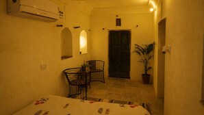 Una habitación con una cama, una mesa con sillas, una planta en maceta, una puerta y un equipo de aire acondicionado.