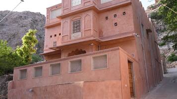 Un edificio rosa con diverse finestre e un'apertura, posto su una superficie pavimentata con uno sfondo roccioso.