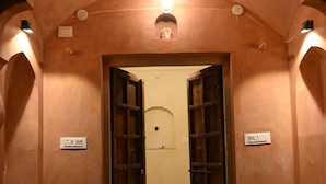 Un pasillo con una puerta que da a una habitación, una lámpara sobre la puerta y un interruptor en la pared.