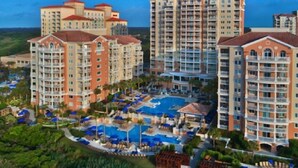 Un hotel con diversi edifici a grattacielo, una piscina centrale con lettini e un giardino curato.