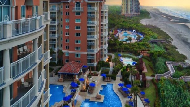 Un hotel con piscina, diversi balconi e vista sulla spiaggia.
