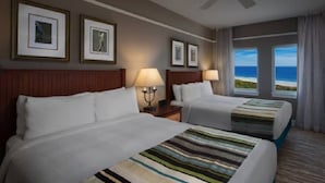 Camera d'albergo con due letti, una ventola a soffitto, quadri appesi alle pareti e vista sull'oceano.