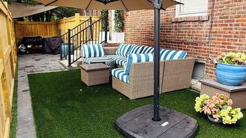 A patio area with outdoor furniture, a covered seating area, and a brick building in the background.