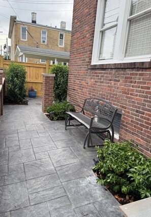 En belagt terrasse med en bænk, en murstensvæg og et træhegn.