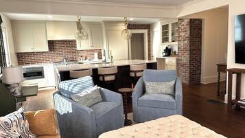 A modern living room with a fireplace, a kitchen with a brick backsplash, and a dining area with bar stools.