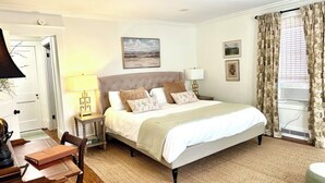 Quarto com cama, mesas de cabeceira, luminária, cadeira e porta.