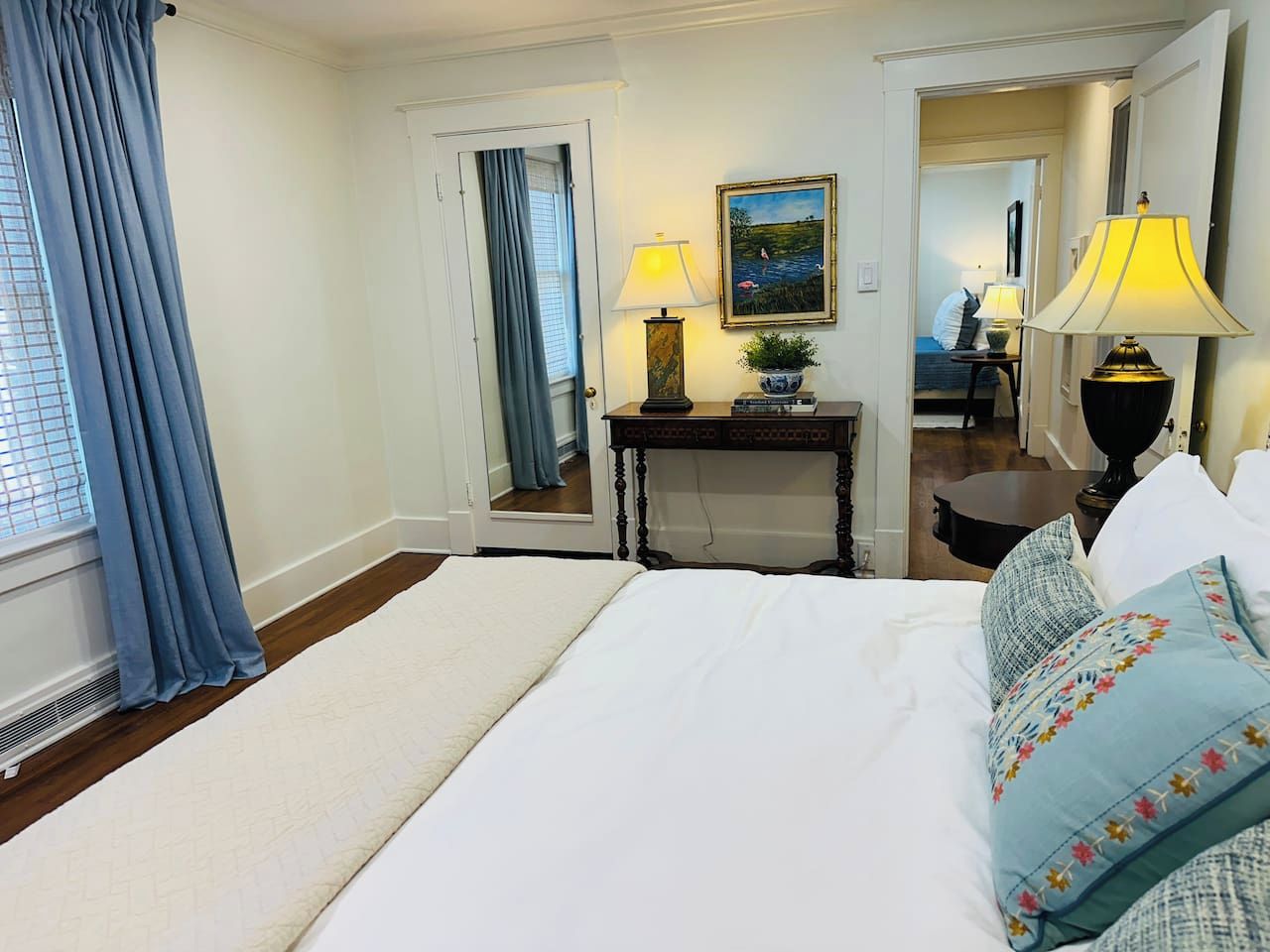 Habitación de hotel con una cama grande, dos lámparas de noche, una mesita de noche, un cuadro y un espejo.