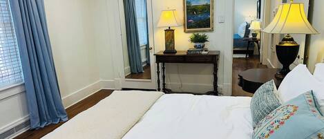 Habitación de hotel con una cama grande, dos lámparas de noche, una mesita de noche, un cuadro y un espejo.