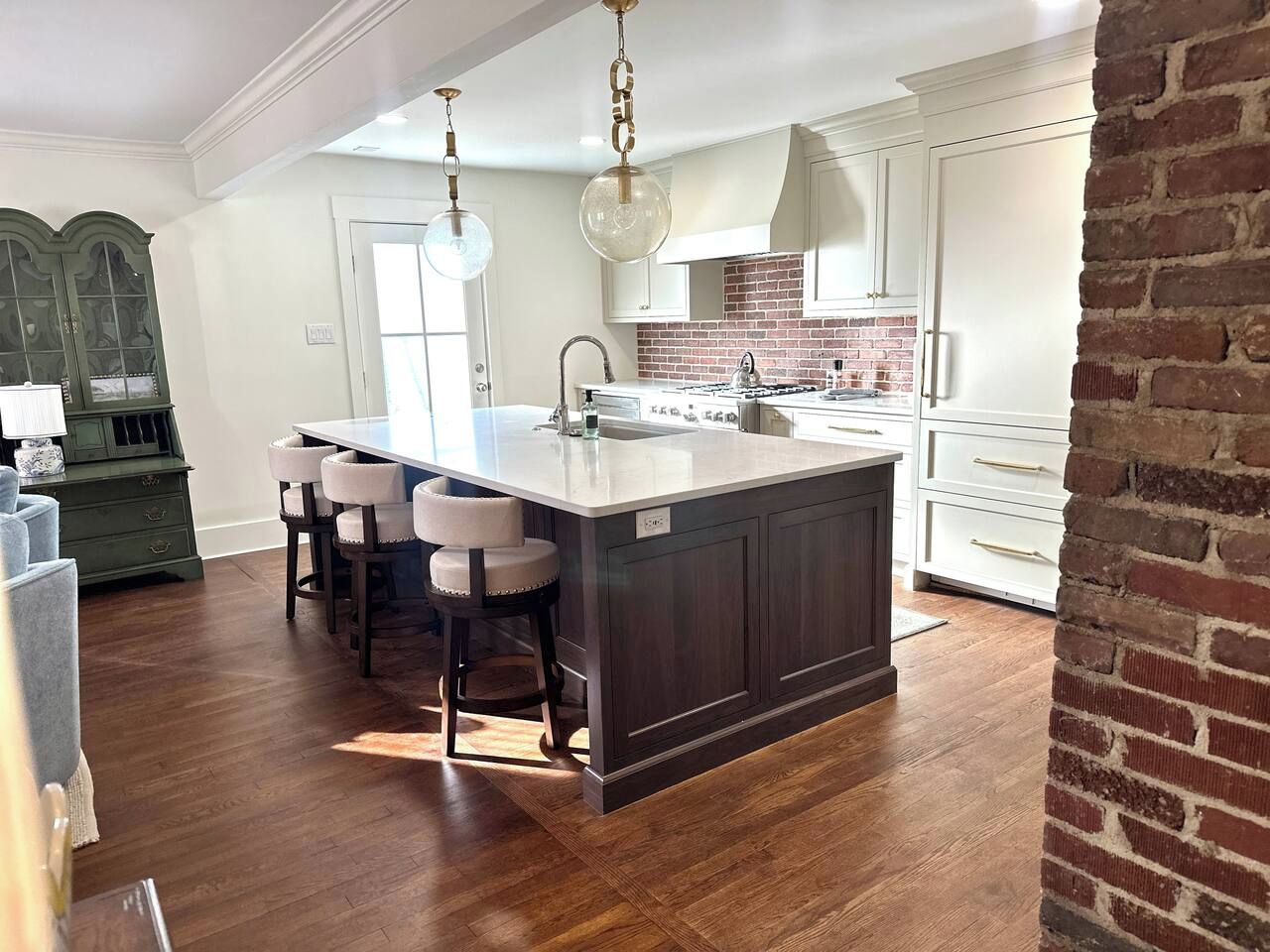 A kitchen with a large island, white cabinets, and a brick accent wall.