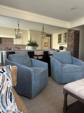 A modern living room with two blue armchairs, a beige sofa, and a kitchen in the background.