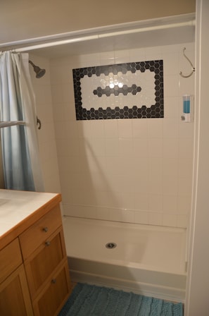 A bathroom with a shower, a tiled wall, a wooden cabinet, and a blue rug.