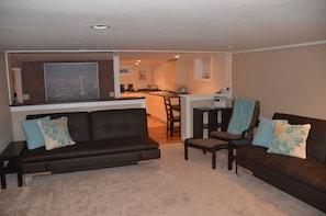 A living room with a brown leather sofa, a dining table, and a kitchen in the background.