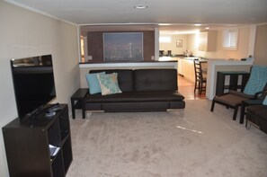 A living room with a sofa, a TV, and a kitchen in the background. - Spacious Family-Friendly Phinney Flat Near Zoo (Seattle)