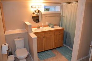 A bathroom with a toilet, sink, wooden cabinets, a mirror, a towel rack, and a shower curtain. - Spacious Family-Friendly Phinney Flat Near Zoo (Seattle)