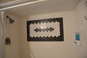 Eine Dusche mit einem schwarz-weißen, sechseckigen Fliesenspiegel, einer Handbrause und einem Seifenspender an der Wand.