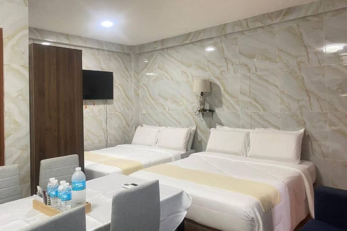 Una habitación de hotel con dos camas, un escritorio con silla, un televisor de pantalla plana y una pared con diseño de mármol.