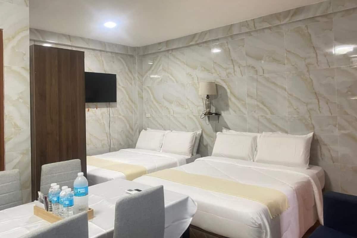 A hotel room with two beds, a desk with a chair, a flat-screen TV, and a marble-patterned wall.