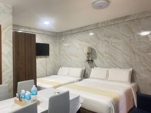 Ein Hotelzimmer mit zwei Betten, einem Schreibtisch mit Stuhl, einem Flachbildfernseher und einer Wand mit Marmorstruktur.