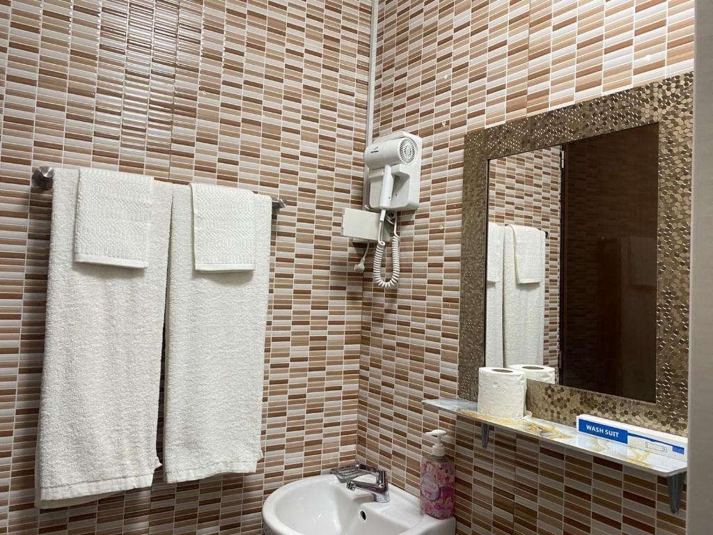 A bathroom with a tiled wall, a sink, a mirror, a hairdryer, and towels.