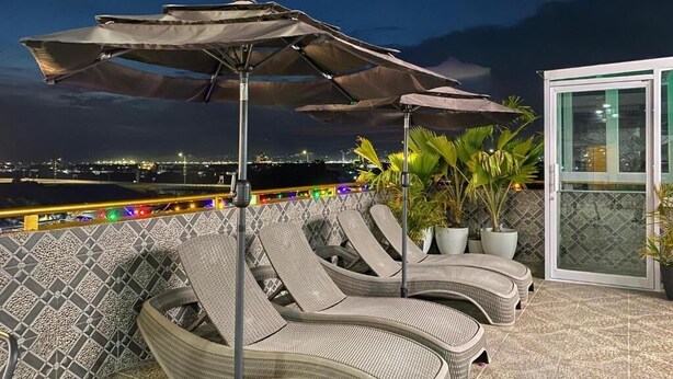 A terrace with lounge chairs and umbrellas, a tiled wall, and a view of the city at night.