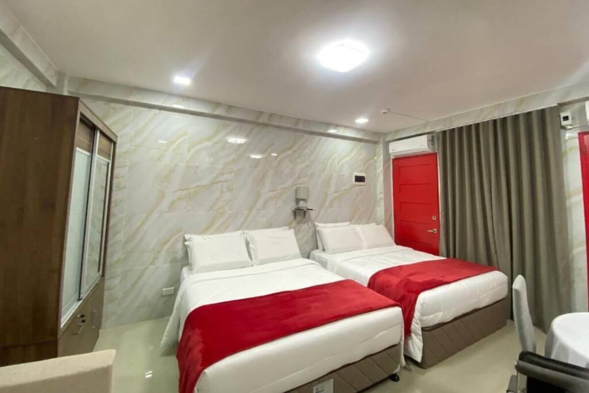 Habitación de hotel con dos camas, un espejo, una puerta roja y una ventana con cortinas.