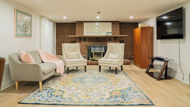 Ein Wohnzimmer mit Kamin, zwei Sesseln, einem Sofa, einem Fernseher und einem gemusterten Teppich.