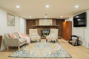 Een woonkamer met een open haard, twee fauteuils, een bank, een televisie en een kamerbreed tapijt.