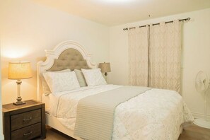 A bedroom with a bed, nightstand, lamp, and curtains. - Spacious 5 bedroom Niagara Falls retreat. Minutes to USA Canada cross border! (Niagara Falls)