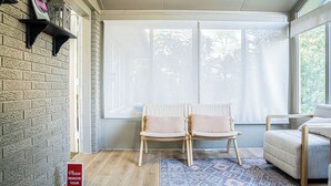 Ein Zimmer mit Backsteinwand, zwei Korbstühlen, einem gemusterten Teppich und einem großen Fenster mit Blick auf Bäume.