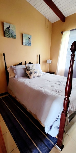 A bed with a wooden headboard, a striped rug, and two wall-mounted paintings. - 2-BR apt in beautiful St Thomas filled with local flava (Charlotte Amalie)