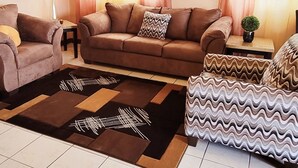 Een woonkamer met een bank, fauteuils, een salontafel en een plafondventilator.