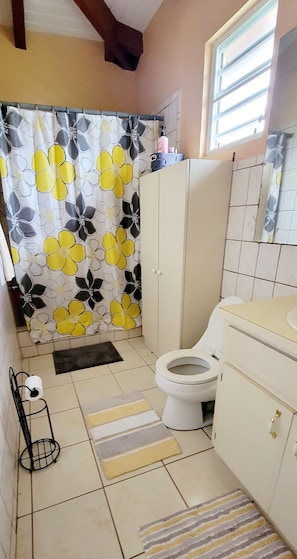 A bathroom with a toilet, a sink, a cabinet, a shower curtain, and a tiled floor. - 2-BR apt in beautiful St Thomas filled with local flava (Charlotte Amalie)