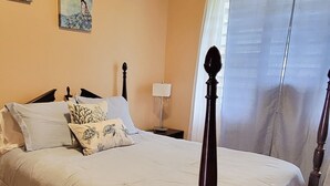 Een slaapkamer met een bed, een plafondventilator, een nachtkastje en een raam met gordijnen.