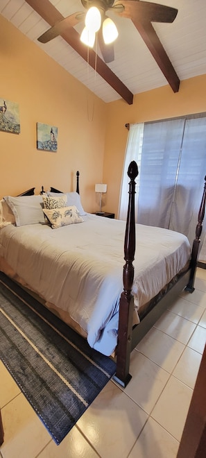 Une chambre à coucher avec un lit, un ventilateur de plafond, une table de chevet et une fenêtre avec des rideaux.