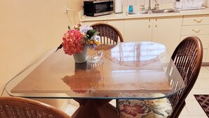 Een eethoek met een tafel met glazen blad, rieten stoelen en een bloevas.