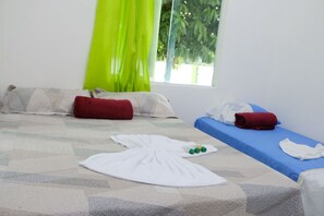 Quarto com uma cama, duas almofadas, um cobertor, uma toalha e uma mesa pequena com garrafas.