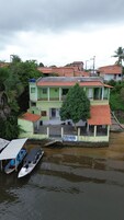 Un edificio de dos plantas con fachada verde y tejado de tejas rojas, junto a una masa de agua con un bote amarrado al frente.