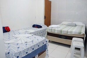Quarto com duas camas, uma porta de madeira e um banquinho branco.
