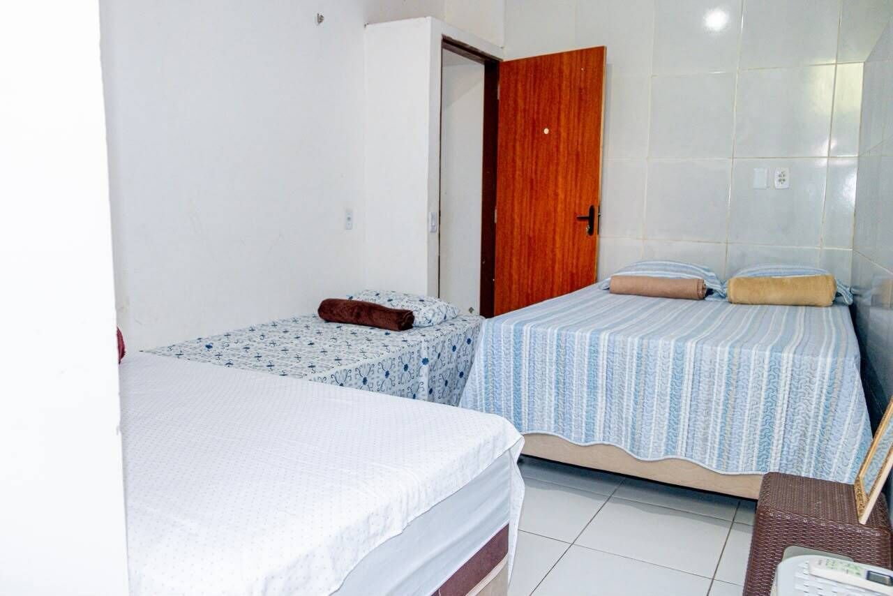 A room with two beds, one with a patterned bedspread and the other with a striped one. There is a wooden door and a white wall.