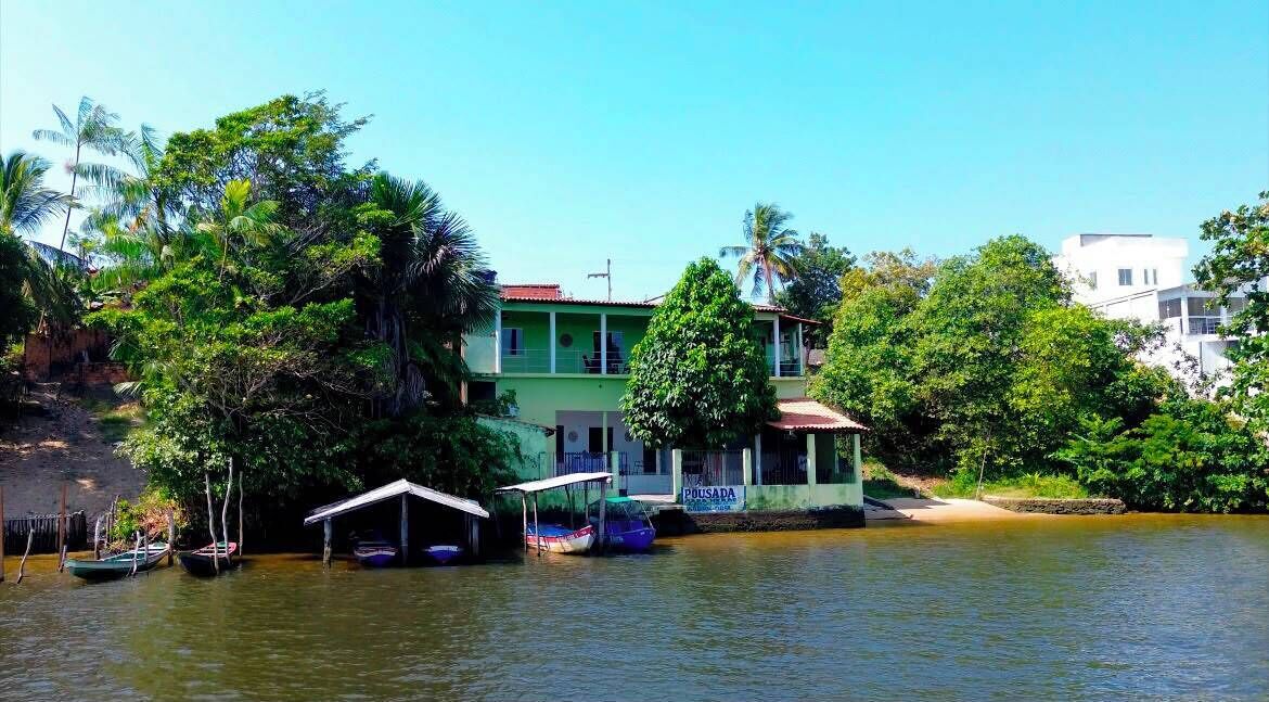 Una propiedad junto al río con un edificio verde, barcos y abundante vegetación.