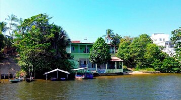Una propiedad junto al río con un edificio verde, barcos y abundante vegetación.