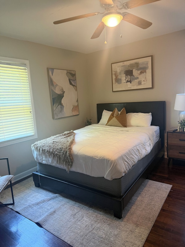 A bedroom with a bed, ceiling fan, artwork, and a window with blinds. - Clark Retreats (Atlanta)