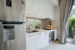 Una cocina moderna con electrodomésticos de acero inoxidable, armarios blancos y un amplio ventanal con cortinas.