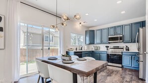 Una cocina moderna con armarios azules, una isla de madera y un comedor con sillas blancas.